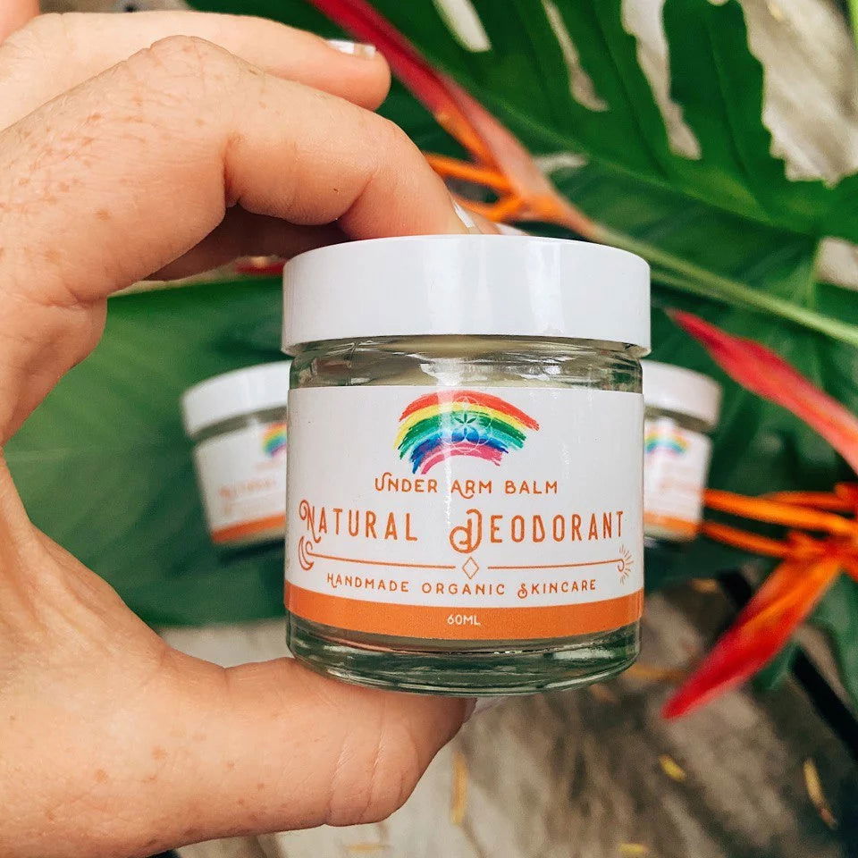 Best natural deodorant in a glass jar, held in hand and displayed among fresh green leaves