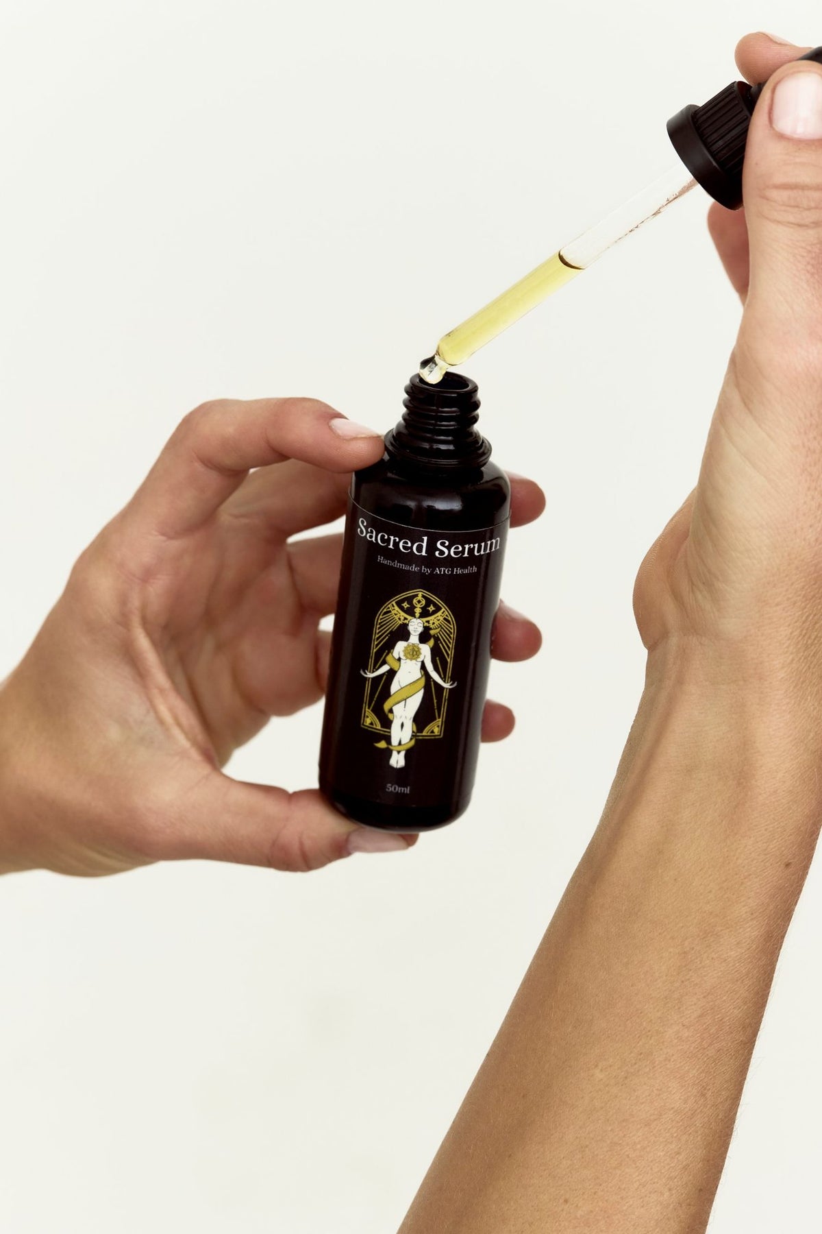 Sacred Serum dropper releasing golden oil into the bottle